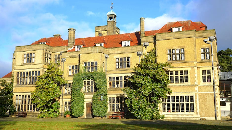 Exterior view of a multi-storey white building with large arched windows framed in yellow, featuring signs for 'SELF STORAGE' and 'BIG YELLOW SELF STORAGE' on the facade. In front of the building, there are smaller houses with tiled roofs, and a few trees partially obscure the lower portion of the structure. A tall street lamp is visible to the right. The scene is captured during daylight with a partly cloudy sky, illustrating a commercial storage facility typical for relocation and moving services provided by Man with Van Swiss Cottage, supporting home relocation and furniture transport within the area.